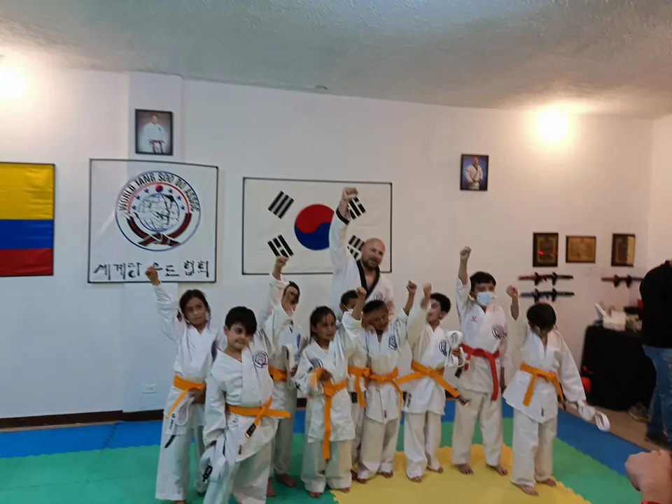 Grupo de niños con cinturones naranja frente a las banderas